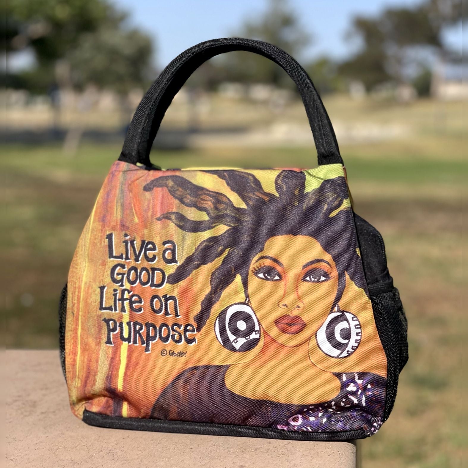 4 of 7: Live Life on Purpose Insulated Lunch Bag Set with Food Containers - Bag with a design of a woman's face and the text 'Live a Good Life on Purpose' in an outdoor setting. (Lifestyle 3)