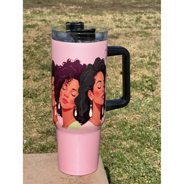 Alpha Kappa Alpha Ivy Love Sisterhood Tumbler with Handle (Lifestyle) - A pink travel tumbler with a black handle and lid, featuring an illustration of three women with dark hair, sitting outdoors on a concrete surface with grass in the background.