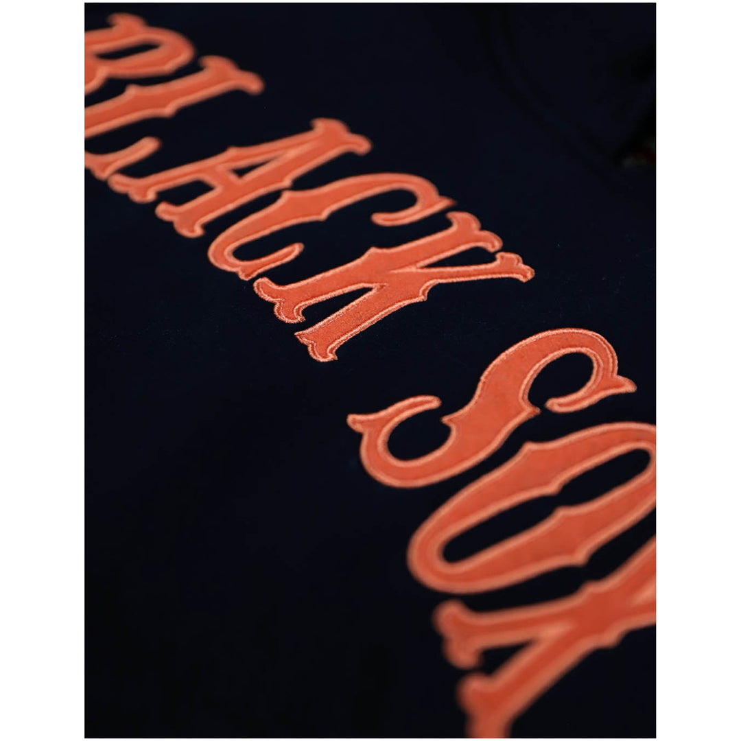 Baltimore Black Sox Heritage Hooded Sweatshirt (Front Detail) - Close-up of a black sweatshirt featuring a large, stylized orange embroidered graphic spelling out 'BLACK SOX'.