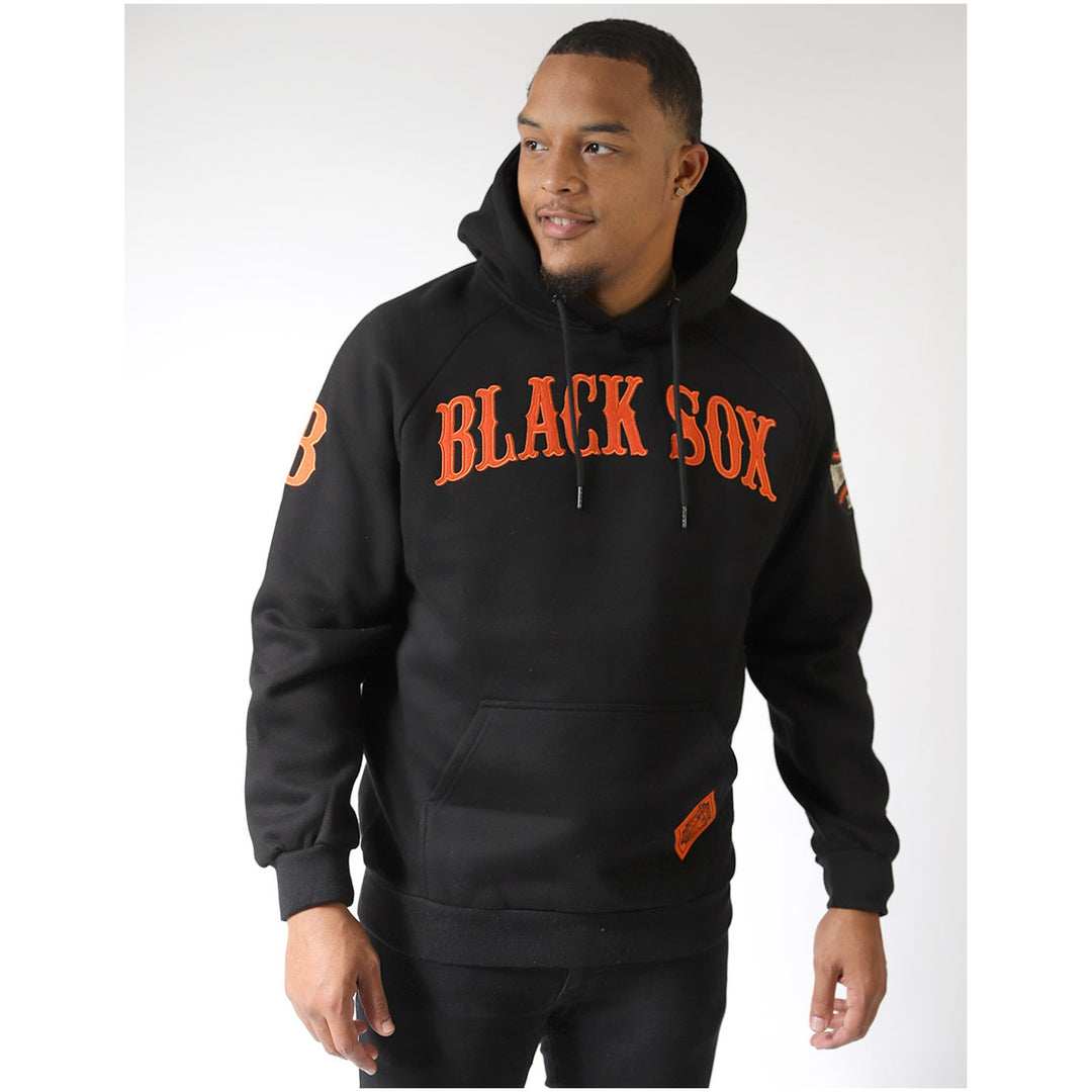 Baltimore Black Sox Heritage Hooded Sweatshirt (Lifestyle) - A man wearing a black pullover hoodie with 'BLACK SOX' printed in orange across the chest, photographed against a light gray studio background.