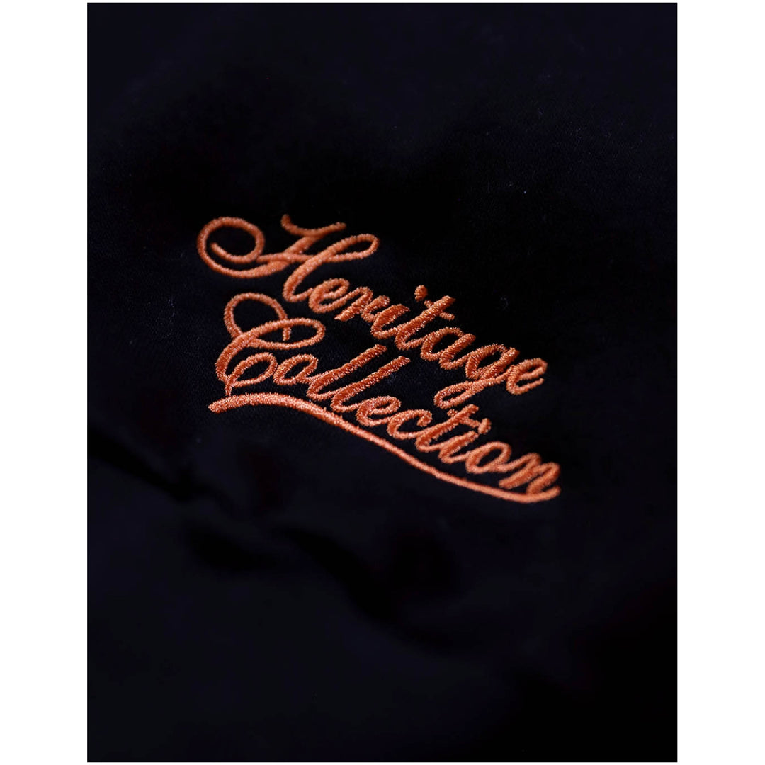 Baltimore Black Sox Heritage Hooded Sweatshirt (Front Detail 3) - Close-up of a black fabric surface with elegant copper-orange embroidered script reading 'Heritage Collection'.