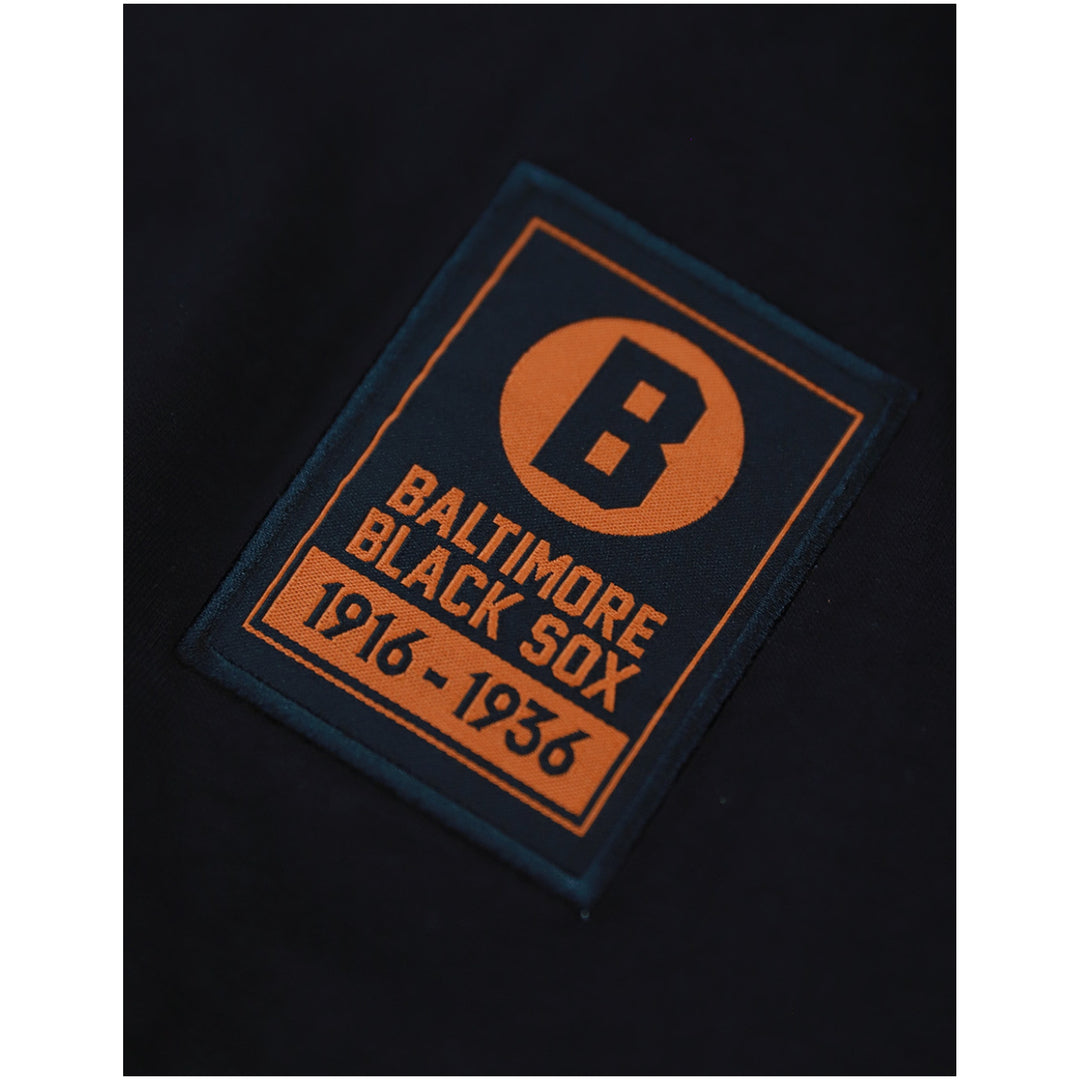 Baltimore Black Sox Long Sleeve T-Shirt (Front Detail 2) - A close-up of a rectangular embroidered patch on a black garment. The patch is dark navy blue with orange text and border details, featuring a large letter 'B' inside an orange circle and the words 'BALTIMORE BLACK SOX 1916 - 1936'.