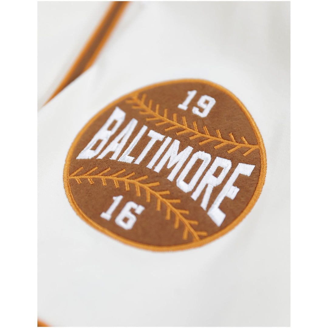 Baltimore Black Sox Negro Leagues Heritage Baseball Jersey (Sleeve Detail) - Close-up of a circular embroidered patch on a white garment, featuring a brown baseball-stitch design with the words 'BALTIMORE' and the numbers 19 and 16 in white.