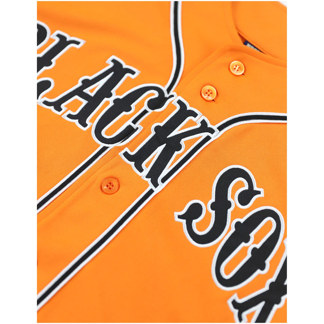 Baltimore Black Sox Legacy Baseball Jersey (Front Detail 2) - Close-up of an orange button-front sports jersey with large black script lettering outlined in white across the chest and sleeves, plus thin black piping.