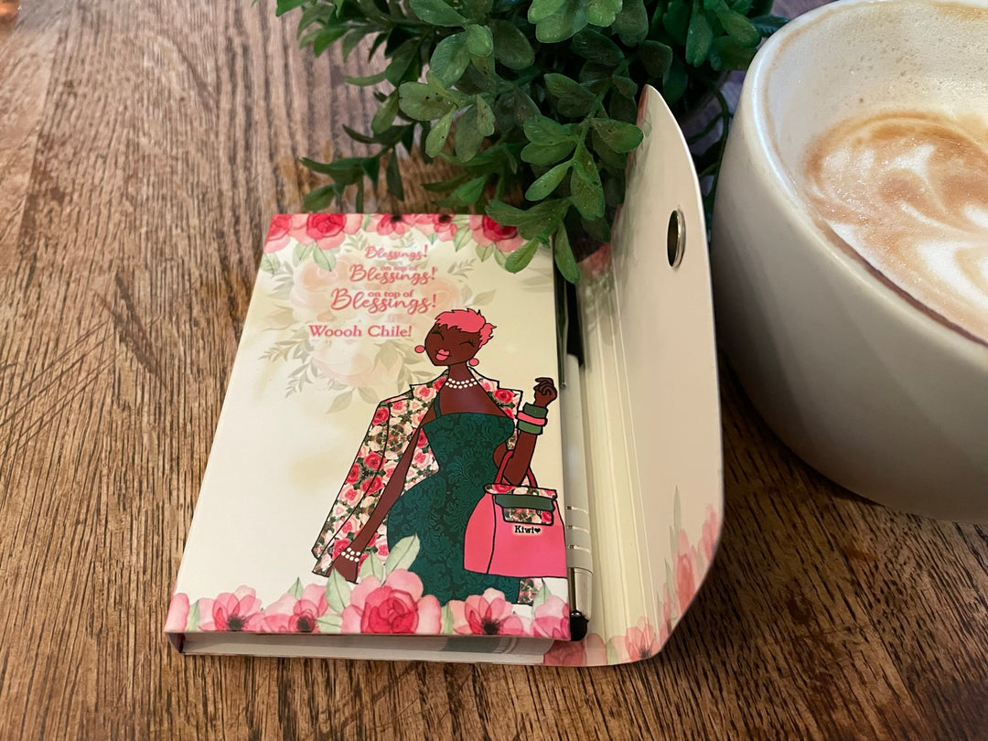 Blessings Upon Blessings (Ivy) Stylus Purse Pal by Kiwi McDowell (Lifestyle) - Notebook with a colorful illustration of a woman on a wooden table next to a cup of coffee and a plant.