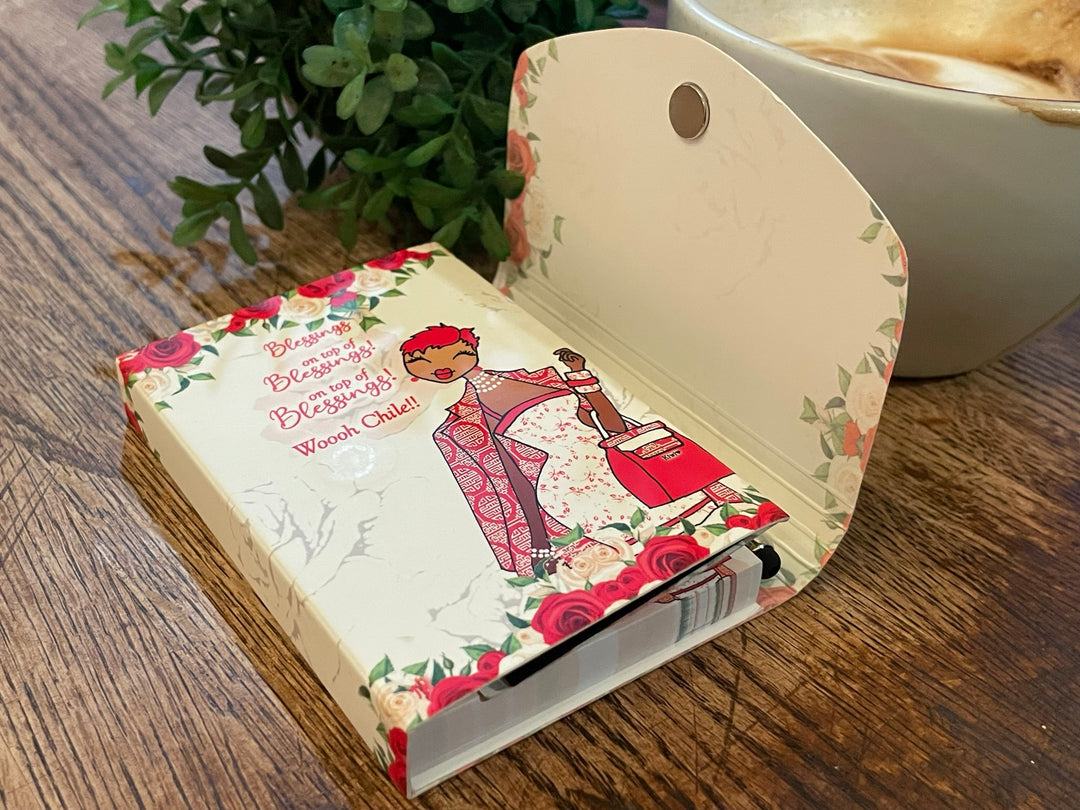 Blessings Upon Blessings (Diva) Stylus Purse Pal by Kiwi McDowell (Lifestyle) - Small notebook with a decorative cover featuring illustrations and text, placed on a wooden surface with a plant and cup in the background.