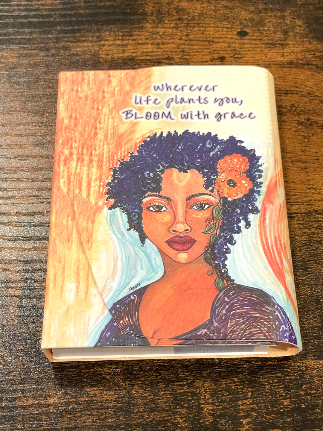 Bloom With Grace: African American Stylus Purse Pal by Sylvia "Gbaby" Cohen (Lifestyle 2) - Notebook with a colorful illustration of a woman with a flower in her hair on a wooden surface.