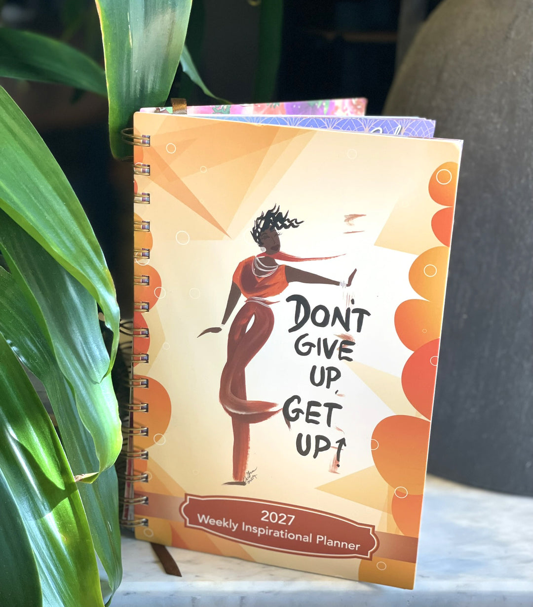 Cidne Wallace Don't Give Up 2027 planner standing beside a green houseplant