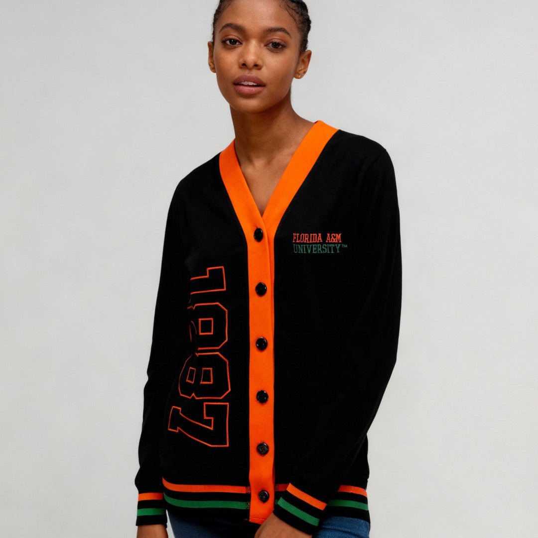 Florida A&M University Rattlers (FAMU) Women's Cardigan (Lifestyle) - A woman modeling a black cardigan sweater with bright orange trim and details, featuring '1987' in orange on the front and 'Tulsa A&M University' embroidered on the chest.