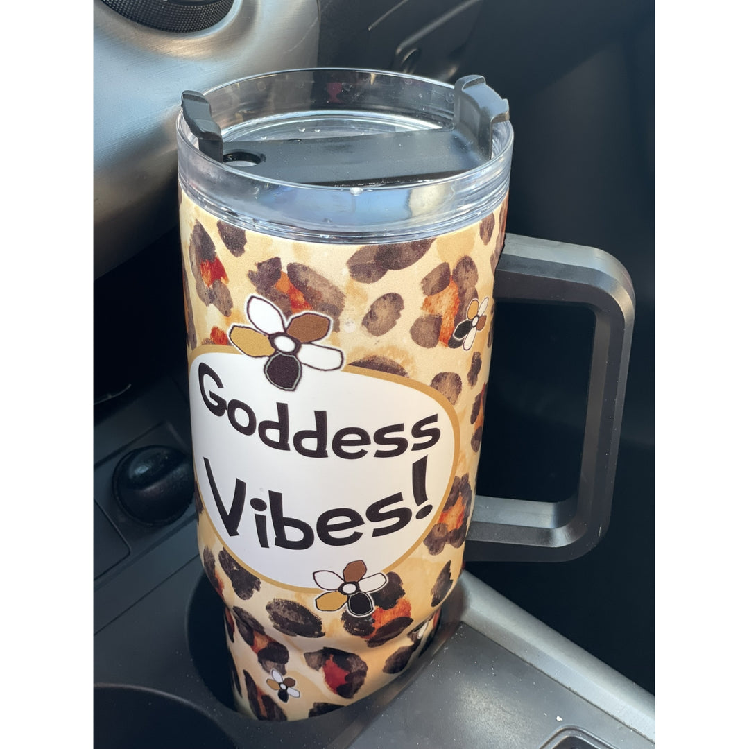 Goddess Vibes by Kiwi McDowell: African American Tumbler with Long Handle (Lifestyle) - A handleless insulated tumbler with a clear lid sits in a car cup holder. The tumbler has a beige and brown leopard print pattern with cartoon bees and a white oval label that reads 'Goddess Vibes!'.