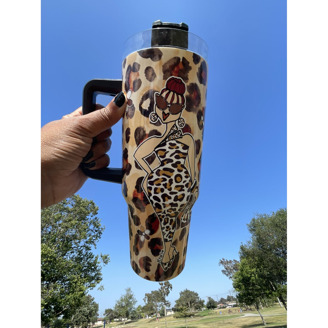 Goddess Vibes by Kiwi McDowell: African American Tumbler with Long Handle (Lifestyle) - A hand with black nail polish holds a tall insulated tumbler with a black handle and lid. The tumbler has a beige leopard print background with a stylized illustration of a woman in a leopard-print dress.