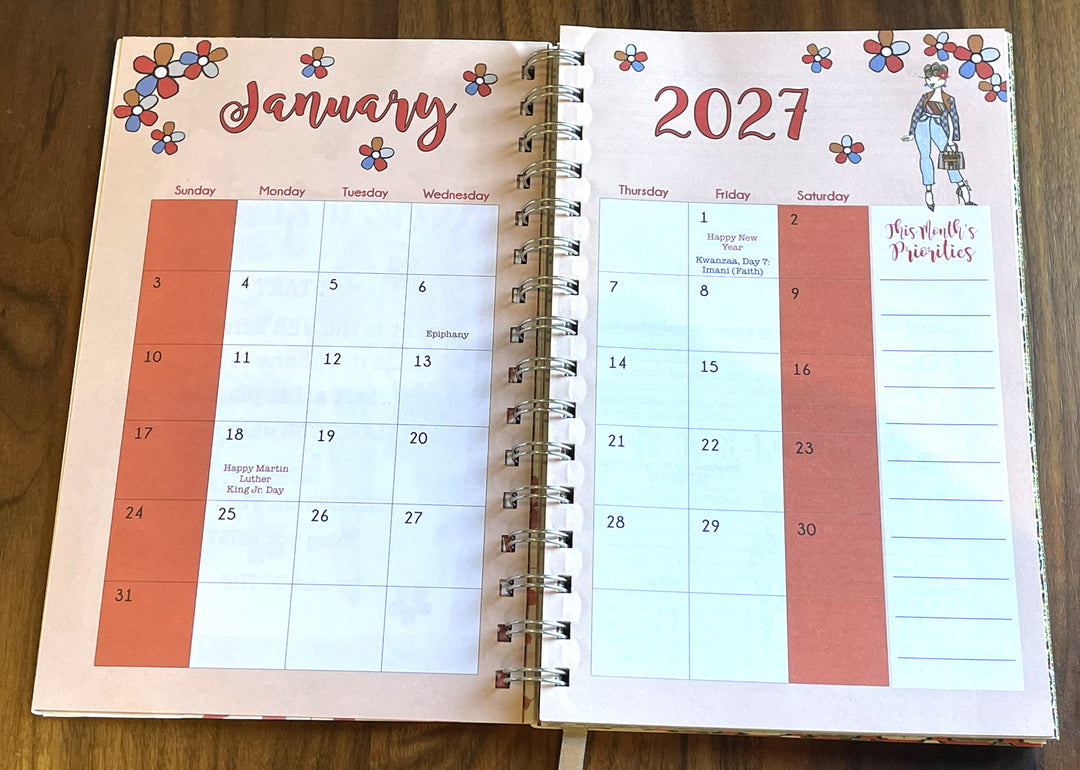 Good Vibes & Voice Mails 2027 Weekly Inspirational Planner by Kiwi McDowell (Monthly View) - An open spiral-bound planner showing the January 2027 page spread on a wooden tabletop. The planner has a pink cover with floral accents and a calendar layout with highlighted dates in coral red.