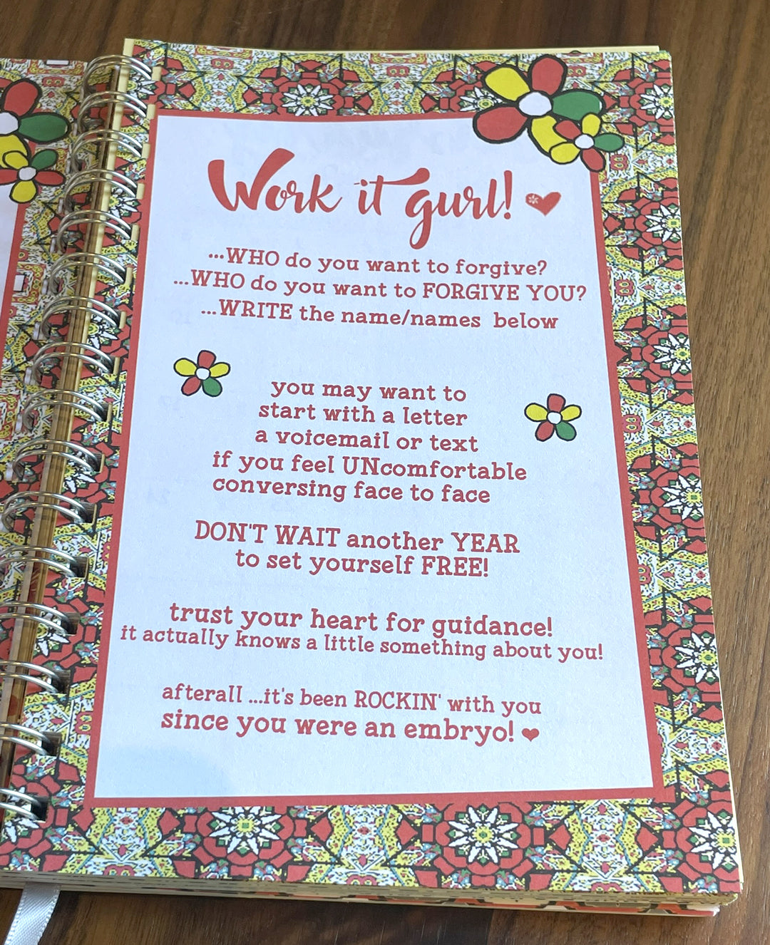 Good Vibes & Voice Mails 2027 Weekly Inspirational Planner by Kiwi McDowell (Interior Pages) - A close-up of a spiral-bound journal or notebook showing a floral-patterned cover and an open page with pink text that reads 'Work it gurl!'.