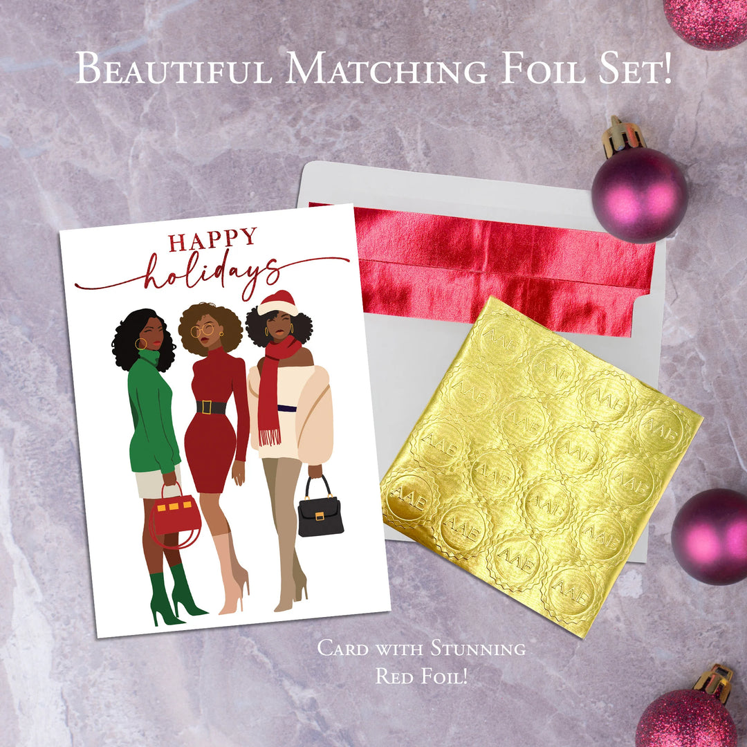 Happy Holidays: African American Christmas Card Box Set (Infographic) - Holiday card with three illustrated women, red foil envelope, and gold foil sheet on a textured surface.