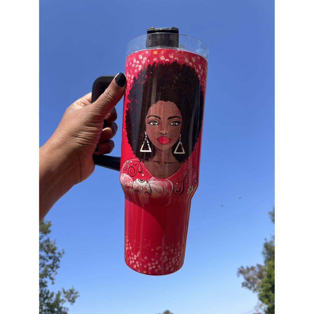 I am Powerful by Sylvia "GBaby" Cohen: Detla Sigma Theta Tumbler with Handle (Lifestyle) - A hand holds a tall insulated tumbler with a black handle and clear lid against a bright blue sky. The tumbler is red with a printed illustration of a Black woman with an afro, pink patterned clothing, and white circular accents.