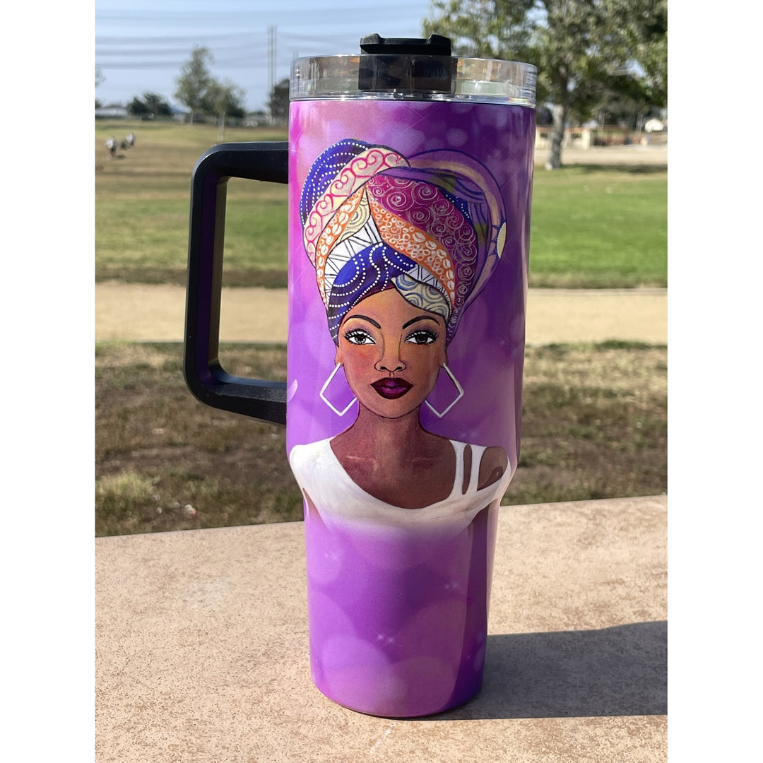 I am Royal by Sylvia "GBaby" Cohen: African American 40 Ounce Tumbler with Long Handle (Lifestyle) - A purple handled tumbler with a black lid, featuring a printed illustration of a woman with a colorful headwrap, set outdoors on a concrete surface with a grassy field in the background.