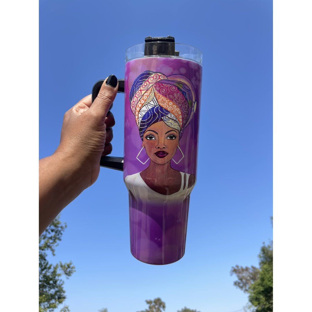 I am Royal by Sylvia "GBaby" Cohen: African American 40 Ounce Tumbler with Long Handle (Lifestyle) - A hand holds a purple insulated tumbler with a black handle and lid against a bright blue sky background. The tumbler features a printed illustration of a woman wearing a colorful patterned headwrap and white earrings.