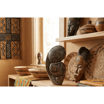 Kissing Lovers: Shona Stone Sculpture by Cuthbert Tendayi (Lifestyle Photo) - A display of African art and decor items in a room with a window.