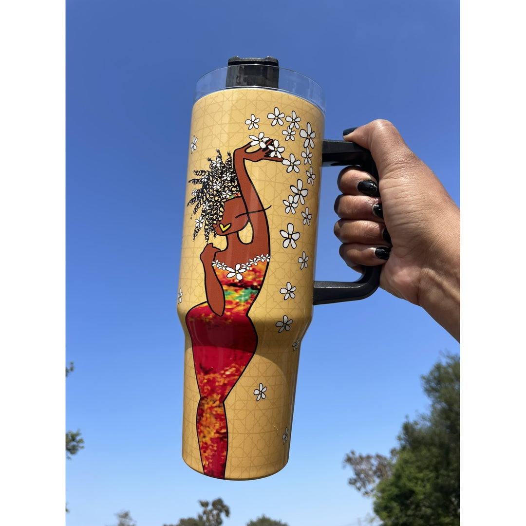 Living My Blessed Life by Kiwi McDowell: African American Tumbler with Long Handle (Lifestyle) - A hand holds a tall insulated tumbler with a black handle against a blue sky background. The tumbler has a tan base with a printed illustration of a woman in a red and multicolor dress surrounded by white flowers.