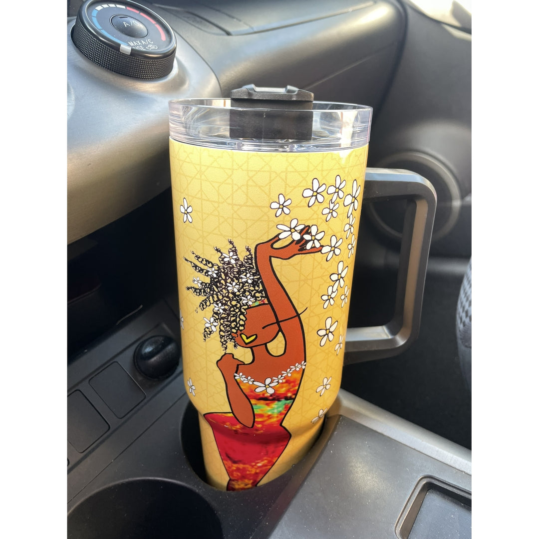 Living My Blessed Life by Kiwi McDowell: African American Tumbler with Long Handle (Lifestyle) - A yellow insulated tumbler with a handle and clear lid sits in a car cup holder. The tumbler features a printed illustration of a woman with an afro holding white flowers, with a red and green patterned skirt.