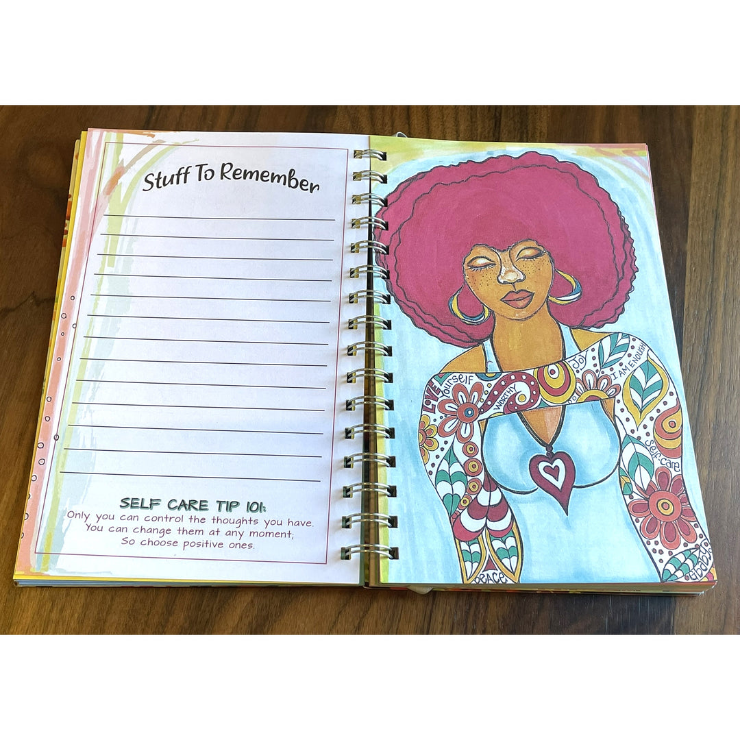 Love Yourself 2027 Weekly Inspirational Planner by Sylvia "Gbaby" Cohen (To Do List) - An open spiral-bound notebook lying on a wooden surface, showing a lined 'Stuff to Remember' page on the left and a colorful illustration of a woman with an afro on the right.