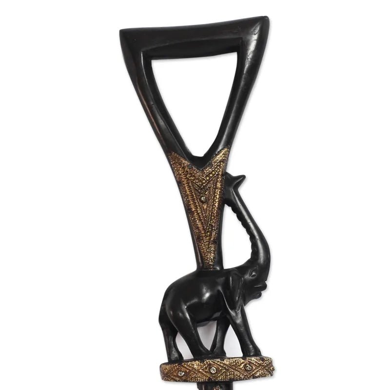 Loyalty and Community (Strolling Elephant): Decorative African Wooden Walking Stick (Front, Detail) - A decorative wall hanging sculpture featuring a black elephant carrying a large inverted triangle frame, with ornate gold geometric patterns on the shaft and base, shown against a plain white background.