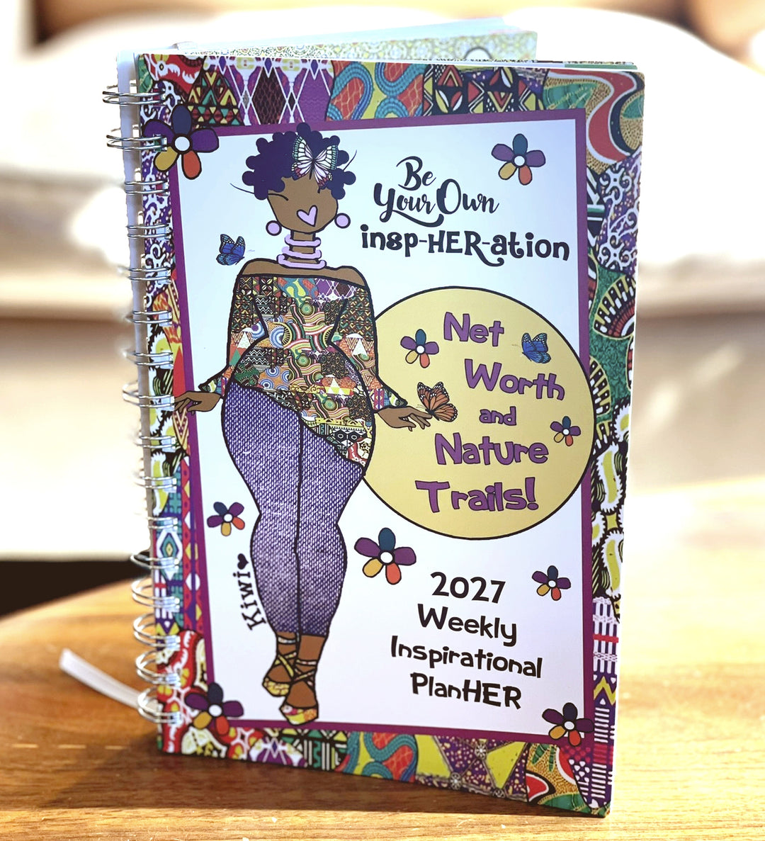 Net Worth and Nature Trails 2027 Weekly Inspirational Planner by Kiwi McDowell (Lifestyle) - A 2027 Weekly Inspirational Planner with a colorful, patterned cover featuring a stylized illustration of a woman and butterflies. The cover includes the text 'Be Your Own inep-HERation', 'Not Worth and Nature Trail!', and '2027 Weekly Inspirational PlanHER'.