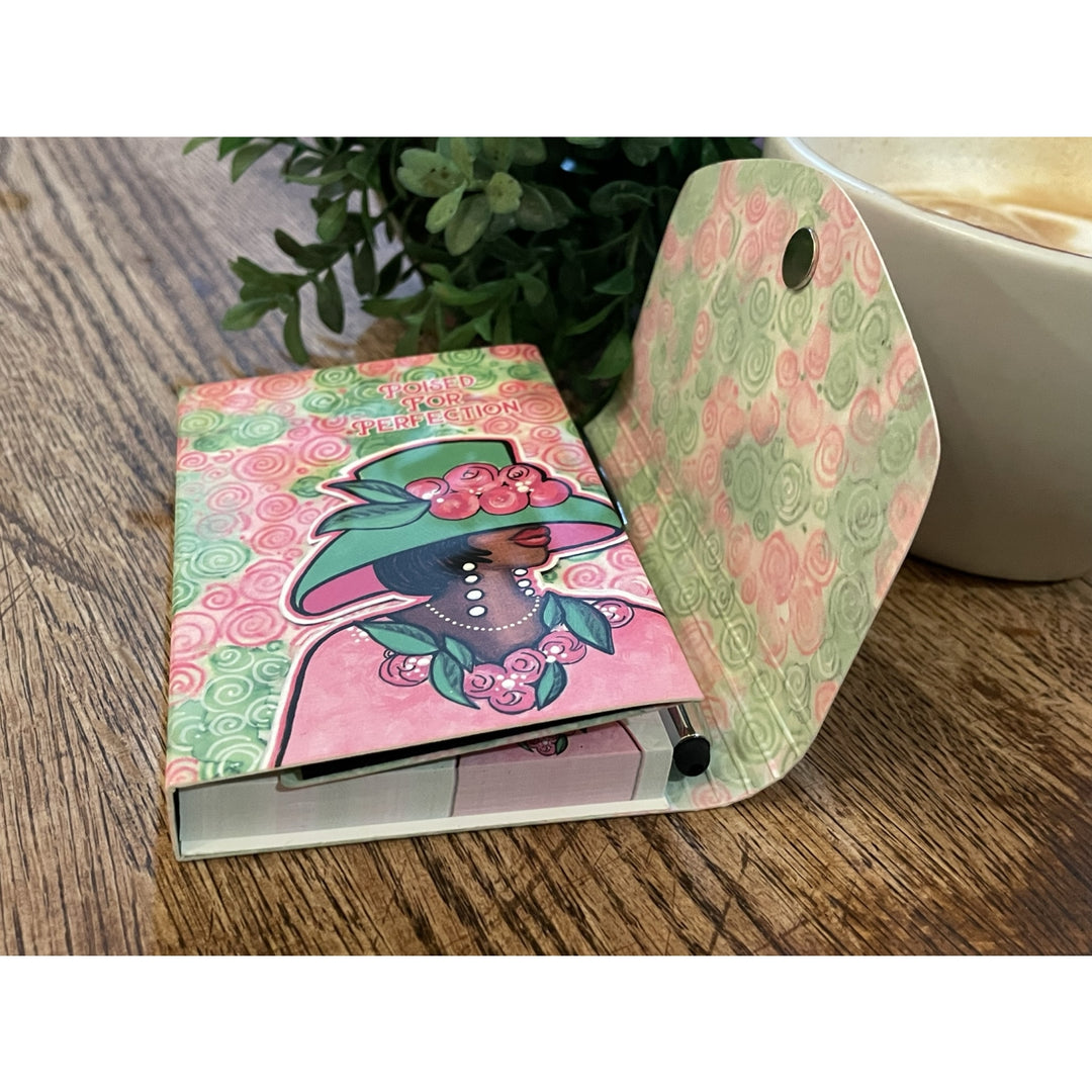 Poised for Perfection (Alpha Kappa Alpha) Stylus Purse Pal by Pamela Hills (Lifestyle) - Notebook with a colorful design on a wooden surface next to a cup.