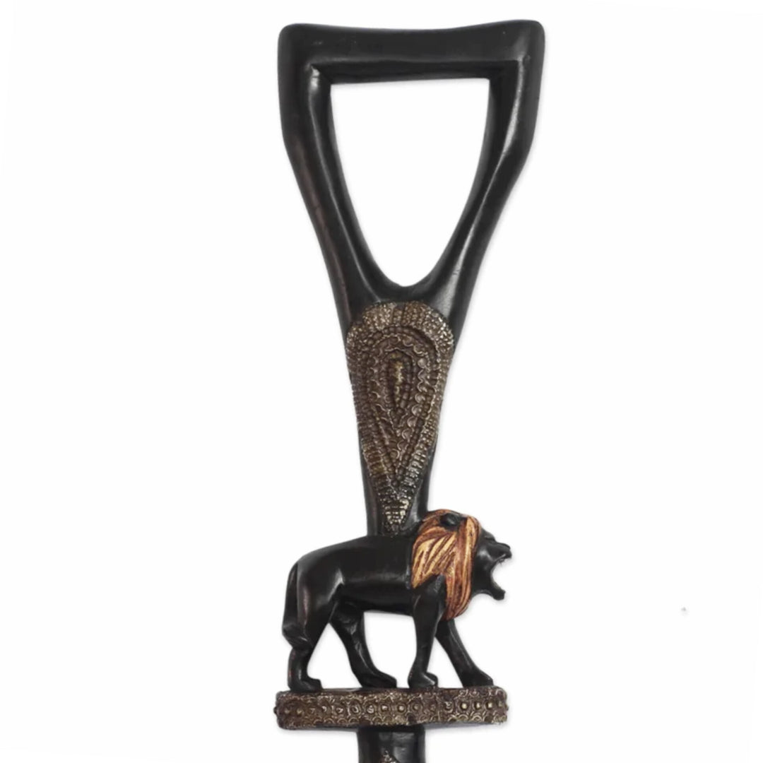 Royalty and Courage (Strolling Lion): Decorative African Wooden Walking Stick (Front, Detail) - A decorative black metal wall hook shaped like a sword hilt, featuring an embossed paisley pattern and a lion figurine at the base with a gold mane, shown against a plain white background.