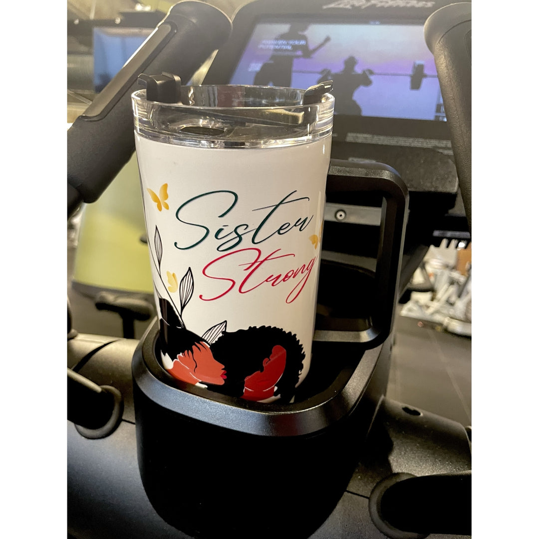 Sister Strong by Janine Robinson: African American 40 Ounce Tumbler with Handle (Lifestyle) - A white insulated tumbler with a clear lid sits in a black gym machine cup holder. The tumbler is printed with the words 'Sister Strong' in teal and red script, decorated with butterflies, leaves, and a black-and-red abstract illustration.