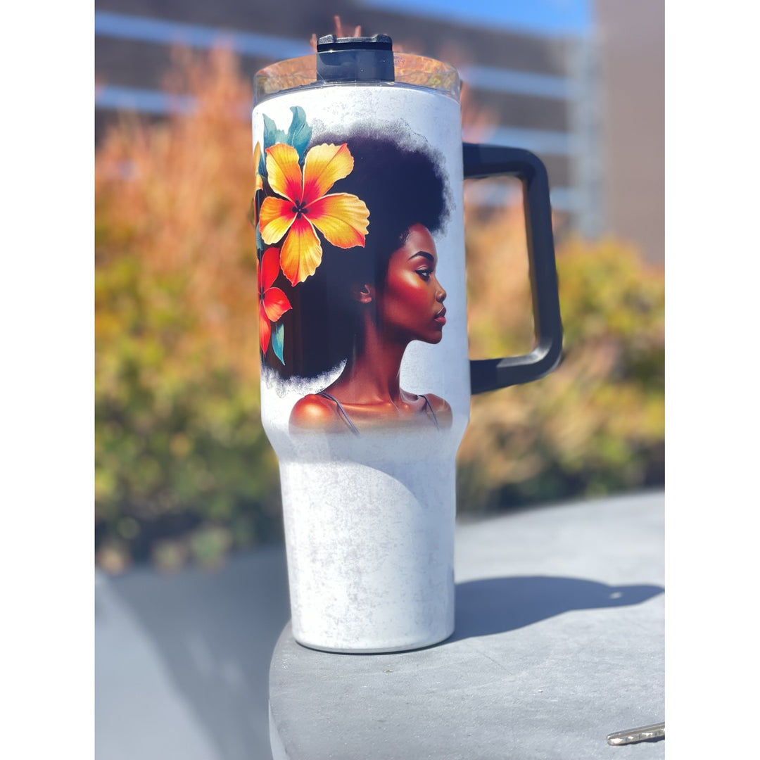 Strong and Special: African American Religious/Faith Tumbler with Handle (Lifestyle) - A white insulated travel tumbler with a black handle and lid, featuring a printed graphic of a Black woman with an afro and a large yellow-orange hibiscus flower, shown outdoors on a gray surface with a blurred background.
