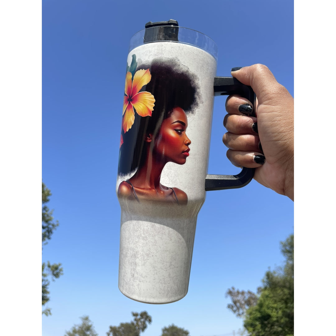 Strong and Special: African American Religious/Faith Tumbler with Handle (Lifestyle) - A hand with black nail polish holds a tall insulated tumbler outdoors against a blue sky. The tumbler has a black handle and lid, a light gray body, and a printed graphic of a Black woman with an afro and a yellow-orange hibiscus flower.