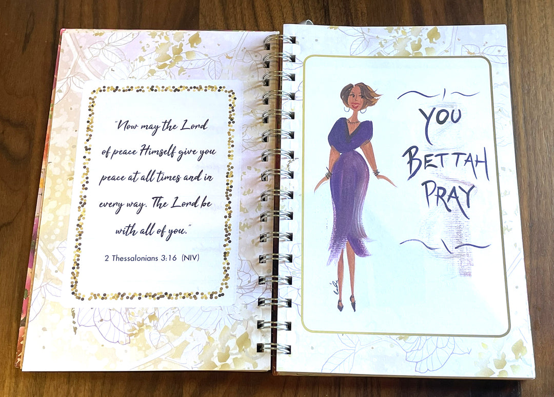 An open spiral-bound prayer journal or notebook laid on a wooden surface. The left page has a decorative border and a Bible verse from 2 Thessalonians 3:16.