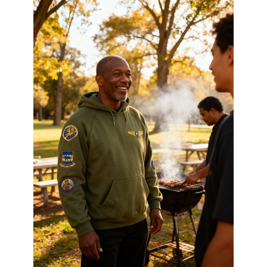 Tuskegee Airmen Squadron Patch Hooded Sweatshirt (Green, Lifestyle) - Man wearing a green hoodie with patches in a park setting, standing next to a grill.
