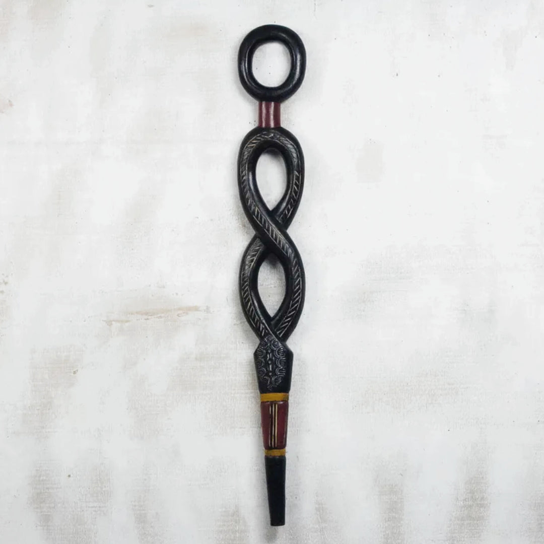Winding Path: Decorative African Walking Stick by Eva Santewa Amakye (Main) - A carved black wooden decorative object with an infinity-like loop design, engraved details, and red and gold painted accents, shown against a light textured fabric background.