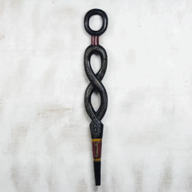 Winding Path: Decorative African Walking Stick by Eva Santewa Amakye (Main) - A carved black wooden decorative object with an infinity-like loop design, engraved details, and red and gold painted accents, shown against a light textured fabric background.